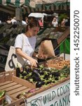 Small photo of London, UK - July, 2019. Young people shopping organic vegetables in a local farmer's market in Brockley, South-East London.