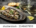 Small photo of Baked snails with butter and spice on dark background. Snails baked with sauce, Bourgogne Escargot Snails. gourmet food. concept of french cuisine, Long banner format. top view.