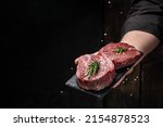 Small photo of Chef salts steak in a freeze motion with rosemary and spices. Preparing fresh beef or pork on a dark background. Long banner format.