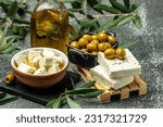 Small photo of feta cheese with olives and olive oil sauce in bowl on dark background. top view. place for text.
