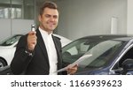 Small photo of A satisfied buyer reread the contract of buying a car. He shows the keys to his new car. He smiles. Men are in the car showroom