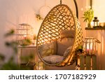 Modern hanging bamboo chair with a cosy beige pillow, candles, lanterns and flowers on a summer evening terrace