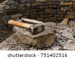 Small photo of Two pound sledge hammer with a pointing chisel resting on a stone in front of a stone wall