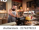 Small photo of Male Indian barista or owner at counter using cashbox computer in cafe store checking client's order. Waiter in apron working in coffee shop. small business, people and service concept