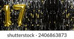 Small photo of Gold foil balloon number number 17 on a background of black tinsel decoration. Birthday card, inscription seventeen. Anniversary event. Banner. copy space.