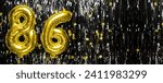 Small photo of Gold foil balloon number number 86 on a background of black tinsel decoration. Birthday greeting card, inscription eighty-six. Anniversary event. Banner. copy space.