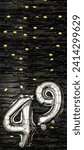Small photo of Silver foil balloon number 49 on a background of black tinsel with gold confetti. Birthday card, inscription forty-ninth. Anniversary event. Vertical banner. copy space.