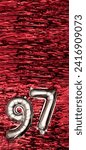 Small photo of Silver foil balloon number 97 on a background of red tinsel decoration. Birthday greeting card, inscription ninety-seven. Anniversary event. Vertical Banner. Copy space