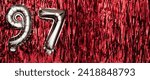 Small photo of Silver foil balloon number ninety-seven. Birthday or anniversary card with the inscription 97. red tinsel background. Anniversary celebration. Banner. copy space
