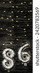 Small photo of Silver foil balloon number eighty-six. Birthday or anniversary card with the inscription 86. Black tinsel background. Anniversary celebration. Vertical Banner. copy space