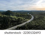 Aerial landscape of 4 lane road with residential area, forest, mountain,  blue sky and sunlight with high angle view of main road from Drone shot in Tak province, northern countryside of Thailand.