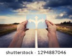 Hands holding paper with arrows crossroad symbol splitted in three different directions. Choose the correct way between left, right and front. Difficult decision concept, over asphalt road background.