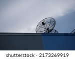 Black satellite TV receiver plate on the roof with a blue sky background.