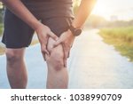 Injury from workout concept : The asian man use hands hold on his knee while running on road in the park. Shot in morning time, sunlight and warm effect with copy space for text or design