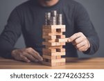 Risks in business or financial concept. Idea to prevent risk in business. Business man playing and selective right or risky piece of tower wooden block game and prevent falling down. Studio shot.