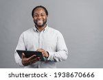 Small photo of Cheerful African-American young man with dreadlocks holding a digital tablet, testing computer app, is surfing in networks, scrolling news feed in social networks, isolated on grey background