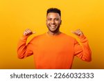 Small photo of This is me. Portrait of proud haughty handsome young man standing, looking at camera and pointing himself. indoor studio shot, isolated on yellow background