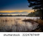 Scenic view of rippled lake with reflection of sunlight against trees and blue sky in forest during sunset