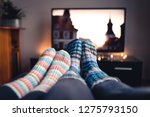 Couple with socks and woolen stockings watching movies or series on tv in winter. Woman and man sitting or lying together on sofa couch in home living room using online streaming service in television