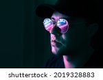 Small photo of Neon reflection in glasses. Man in fluorescent light from city led sign. Mysterious cool model in futuristic cyberpunk portrait. Guy in sunglasses. Techno rave party disco art. Dark black background.