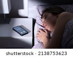 Small photo of Phone call by unknown caller at night while woman is sleeping in bed. Scam, fraud or mobile hoax from suspicious fake number. Illegal mobile crime. Tired person asleep. Stalker or stranger bullying.