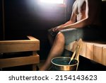 Sauna in Finland. Man relaxing in steam room in health spa, cabin, home or wellness hotel. Traditional Finnish summer. Old wood interior. Water bucket and ladle. Hot temperature therapy.