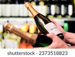 Small photo of Sparkling wine in alcohol store. Champagne or prosecco in liquor shop. Man holding two bottles in hands, choosing drink. Customer compare products in spirits aisle in supermarket. Mockup brand label.