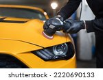 Car detailing and polishing concept. Hands of professional car service male worker, with orbital polisher, polishing yellow luxury car hood in auto repair shop.