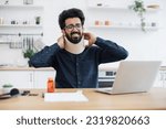 Small photo of Aching mature person touching C collar supporting man's neck while taking break from work because of injury. Indian businessman carrying out professional activity at home despite of constant pain.