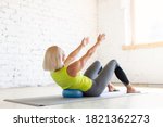 Small photo of Adult caucasian woman practice pilates indoor. Seated rolls up with small fit ball on a mat, abs and back drill, in loft white studio, selective focus. Workout, stretching, fitness, trainer, recovery