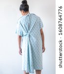 Small photo of A young mixed race African American woman wearing a hospital gown or robe with her back towards camera looks down and leans to the side with her arms limp with a look of discomfort nausea or sadness.