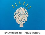 Top view of white drug capsules and yellow pills forming a light bulb with rays on blue background, innovation in medicine, innovative drugs or smart drugs concept