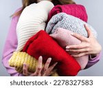 Small photo of A woman holds bright warm winter sweaters. Closet cleaning. Donations. Close-up. Selective focus.