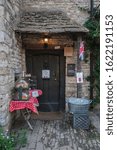 Small photo of CASTLE COMBE, COTSWOLDS, UK - MAY 26, 2018: Beautiful front of old stone cottage with set up table selling home made cakes in the picturesque Castle Combe Village, Chippenham, Cotswolds