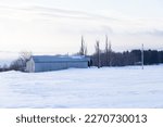 Early morning hazy winter view of large metal-clad grey barn in snowy field, with the St. Lawrence River in the background, St. François, Island of Orleans, Quebec, Canada