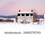 Small photo of Sunrise winter view of beautiful patrimonial brick country house with metal Mansard roof and dormer windows, St. Pierre, Island of Orleans, Quebec