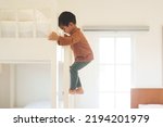 Small photo of Asian little toddler boy is trying to climb up the ladder of bunk bed in the bedroom. Concept of childhood, kid development, physical activity, muscle, playful, learning, life skill for children.