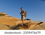 Small photo of A young man travelling on stony area. Landscape photographer with the camera in his hands walking on rocky terrain and wearing backpack