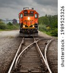 Small photo of Conway, WA, USA - May 14, 2021; An orange BNSF engine approaches a junction switch with headlights on against the gloom