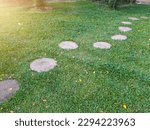 Green lawn and road surface from stone slabs in backyard. Gray color stepping tiles floor, stone path against green grass. Pathway of plated stones with the morning sun 