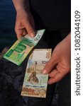 Small photo of Two hands giving odd money, short change. Two new colour paper bills with sevastopol symbols Chersonesus and monument to the scuttled ships. Black, green, brown, white, vertical, bank.