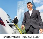 Businessman plugging in the charger in electric car and going to work in business center - skyscraper