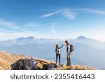 Small photo of Epic view of mountain ridge and range in the haze under the sun and victory gesture high five hands of hiker couple. Motivation, support, love, and success concepts.
