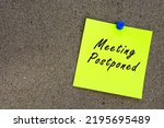 Small photo of Meeting postponed on yellow stick note and pinned to a cork notice board. Reminder and business concept.
