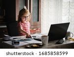 Smart little toddler girl wearing big glasses while using her laptop. Young beautiful girl sitting at working place in home office.