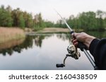 Small photo of Fisherman with rod, spinning reel on the river bank. Man catching fish, pulling rod while fishing from lake or pond with text space. Fishing for pike, perch on beach lake or pond. Fishing day concept.