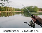 Small photo of Man catching fish, pulling rod while fishing from lake or pond. Fisherman with rod, spinning reel on river bank. Sunrise. Fishing for pike, perch, carp on beach lake or pond. Background wild nature.