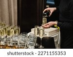 Woman pours champagne into flute glasses. Champaign is being pored into glasses. The waiter pouring white sparkling wine. Bottle in a closeup view. Rows of full glasses. Catering service concept.