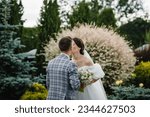 Small photo of Kiss. Newlyweds says promise of fidelity in love in nature. Happy bride and groom exchanging wedding vows on ceremony in backyard banquet area. Couple standing with bouquet outdoors. Back view.