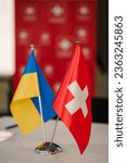 Small photo of Flags of Ukraine and Switzerland. Small flags on table in office of president. Blue and yellow flag. State symbols. Sovereign independent free state. Swiss help, support. Ukraine Recovery Conference.